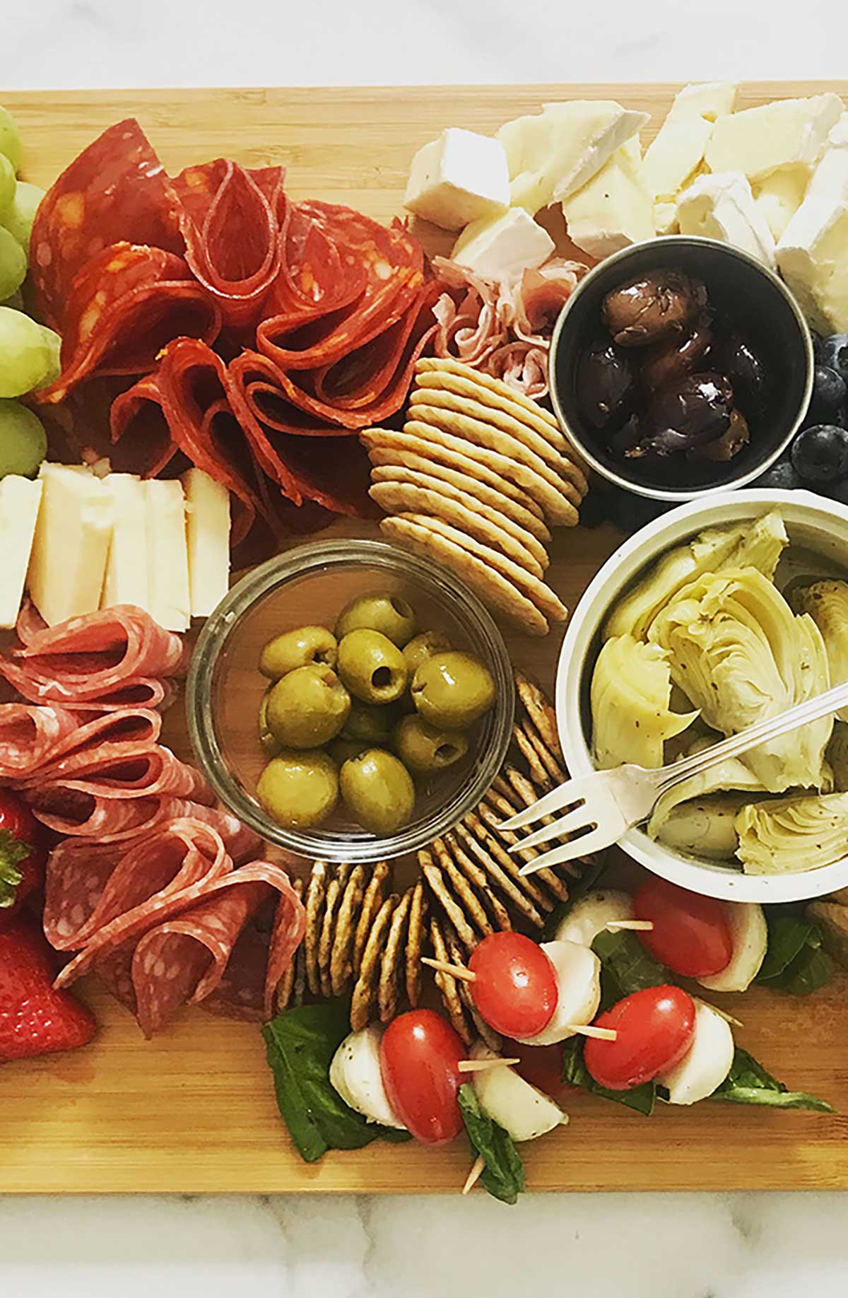 charcuterie board with cheese, salami, crackers on wood board over marble counter