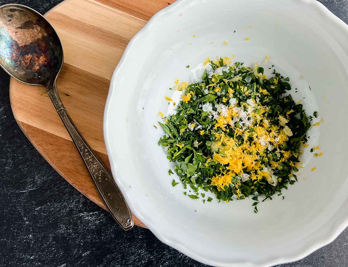 ingredients in a white bowl that include parlsey, lemon zest, salt and garlic all minced in small pieces