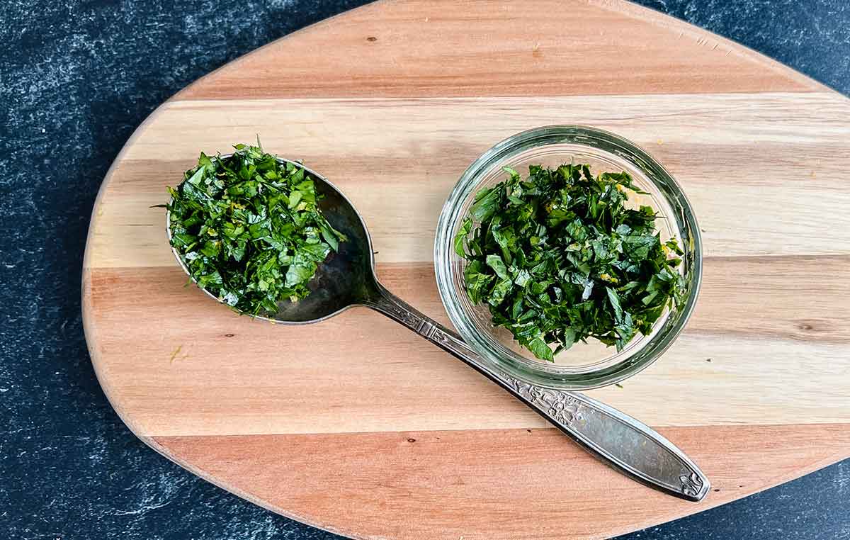 fresh parsley condiment with some on an old metal spoon and some in the small bowl on a cutting board