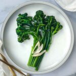 sauteed broccolini on a light gray plate with shallots