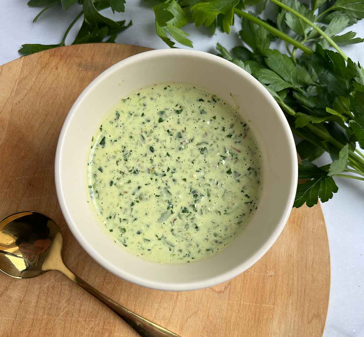 bowl filled with chimichurri aioli and gold spoon and flat leaf parsley in image