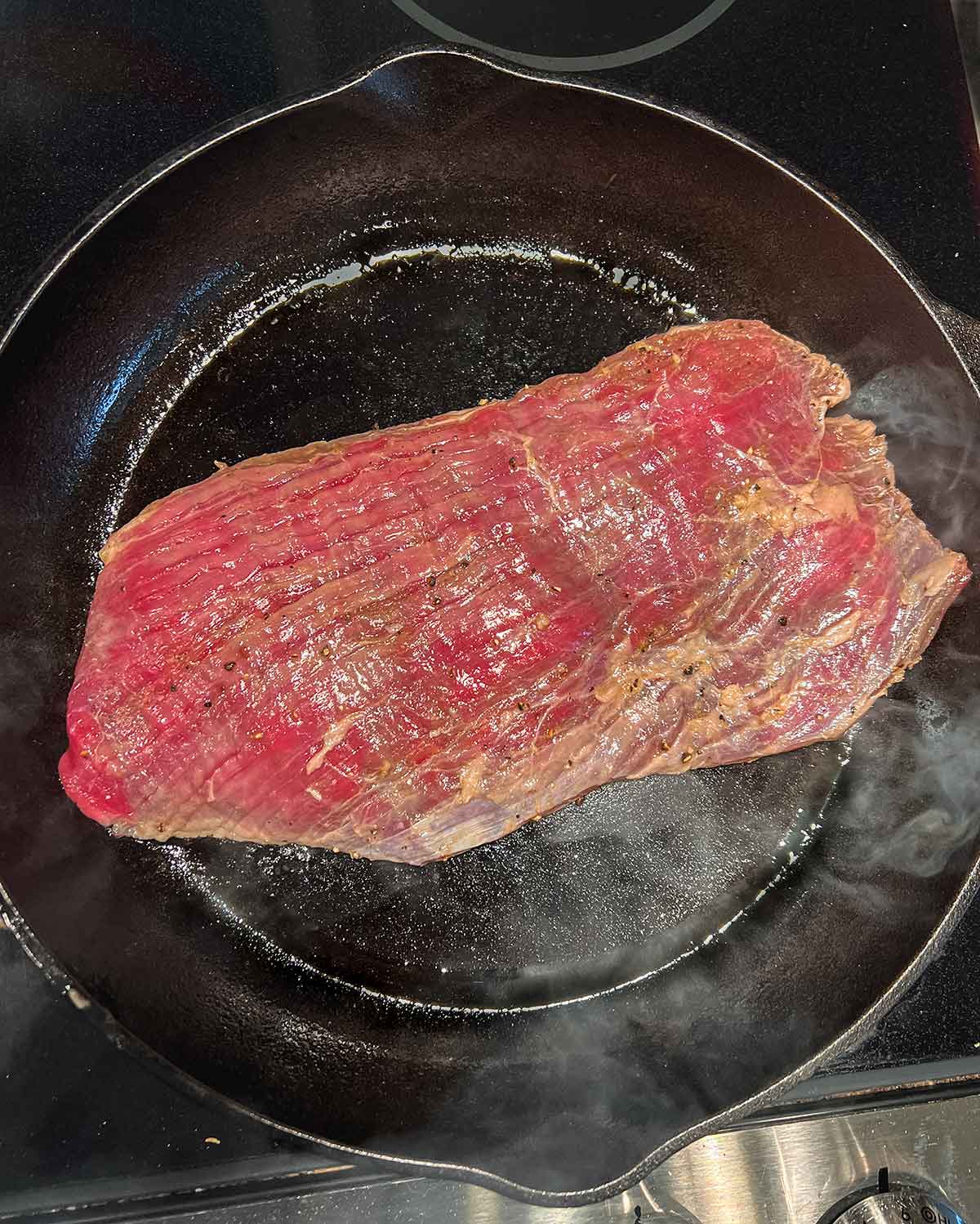 flank steak in black cast iron pan searing