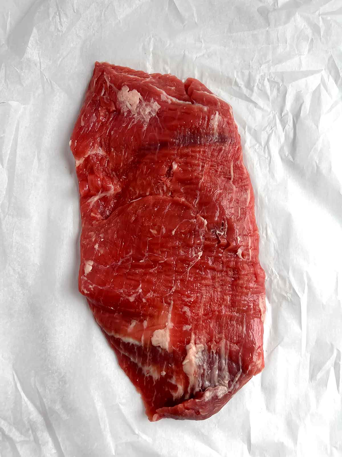 raw flank steak on parchment paper