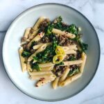 italian sausage and kale penne pasta in shallow bowl on marble countertop