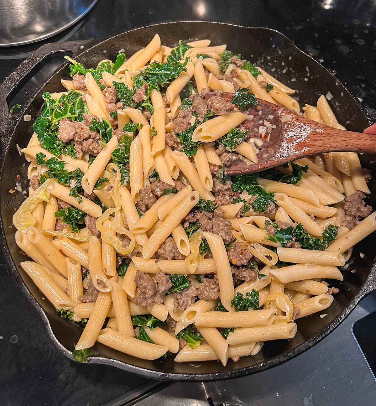 mixing sausage and kale pasta in cast iron pan