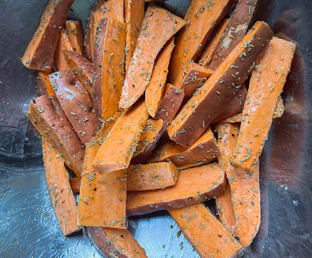 cut sweet potato wedges with skin on with seasoning in metal bowl
