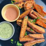 Sweet potato wedges on black plate with dipping sauces and parsley minced on top.