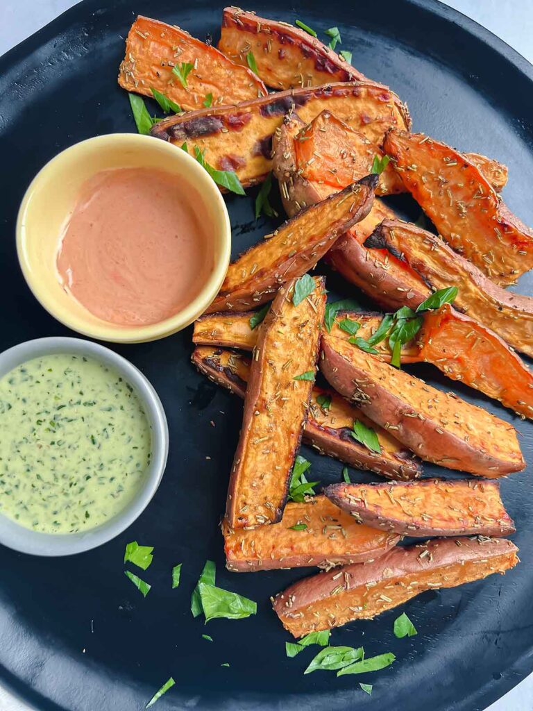 Sweet potato wedges on black plate with dipping sauces and parsley minced on top.