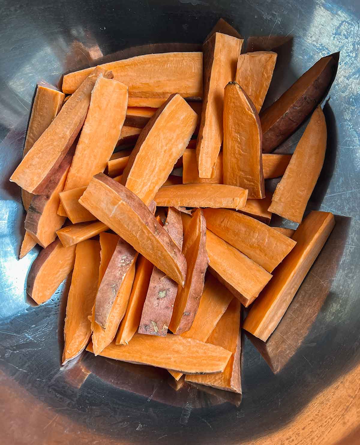 cut sweet potato wedges in metal bowl before seasoning