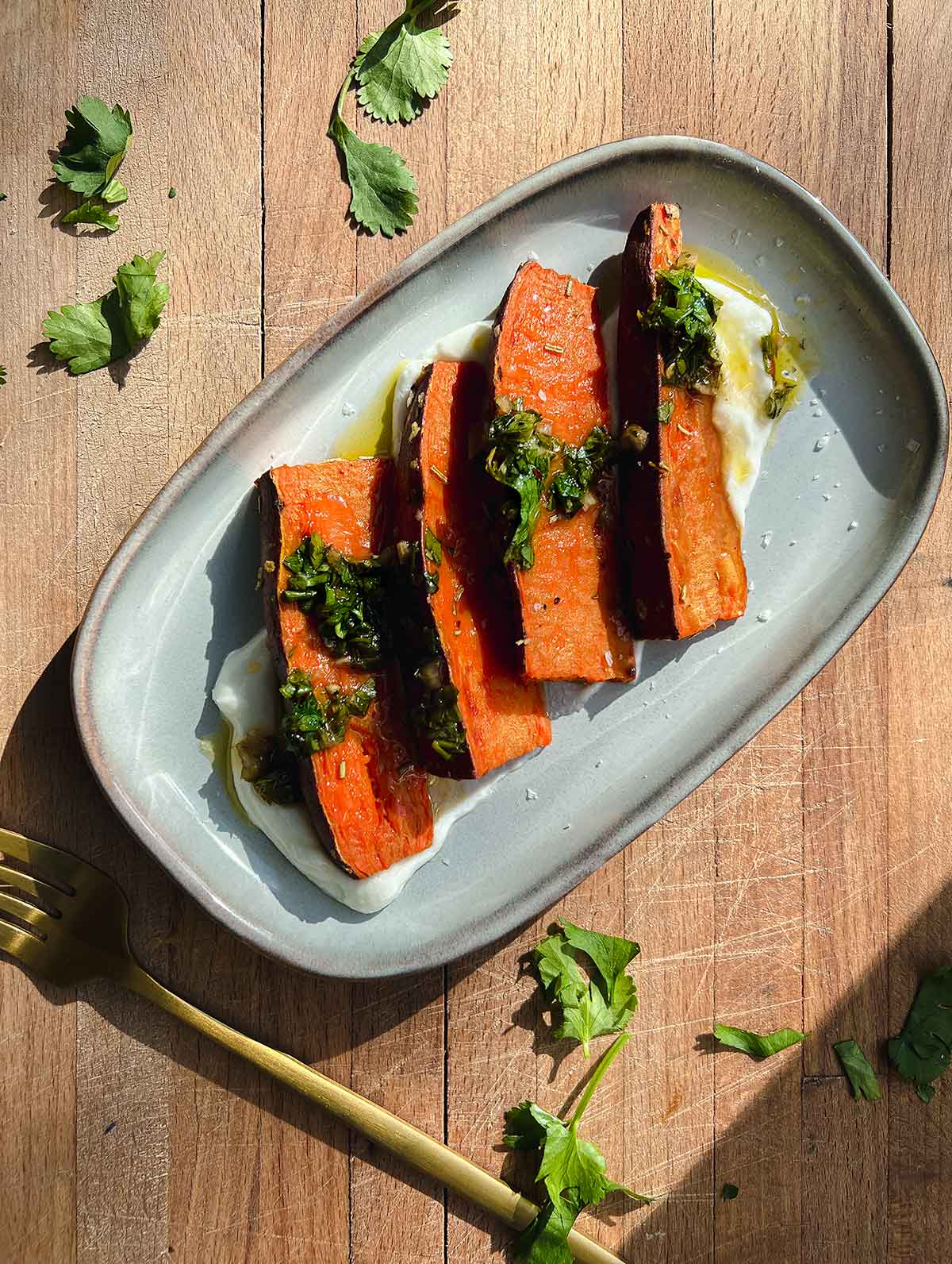 sweet potatoes on gray rectagular plate on bed of strained greek yogurt with chimichurri drizzled on top