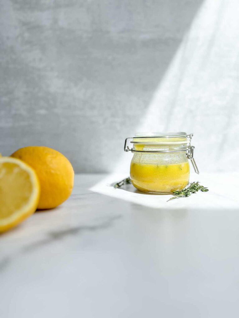 fresh lemon and thyme dressing in small air tight jar on marble counter with white background