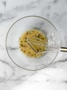mixed lemon herb dressing recipe ingredients in glass bowl using whisk